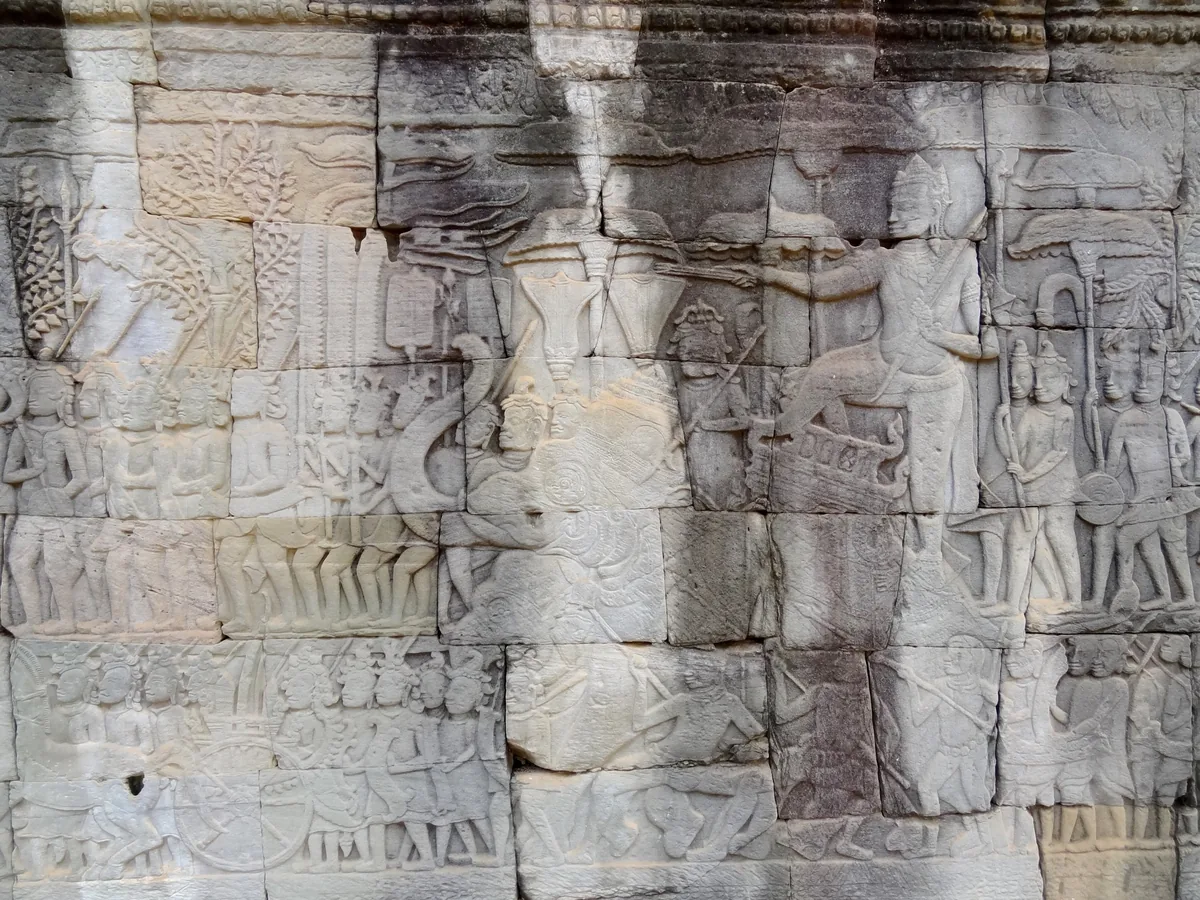 Ancient stone bas-relief carvings depicting figures and battle scenes on a temple wall at Bayon, Angkor Thom.