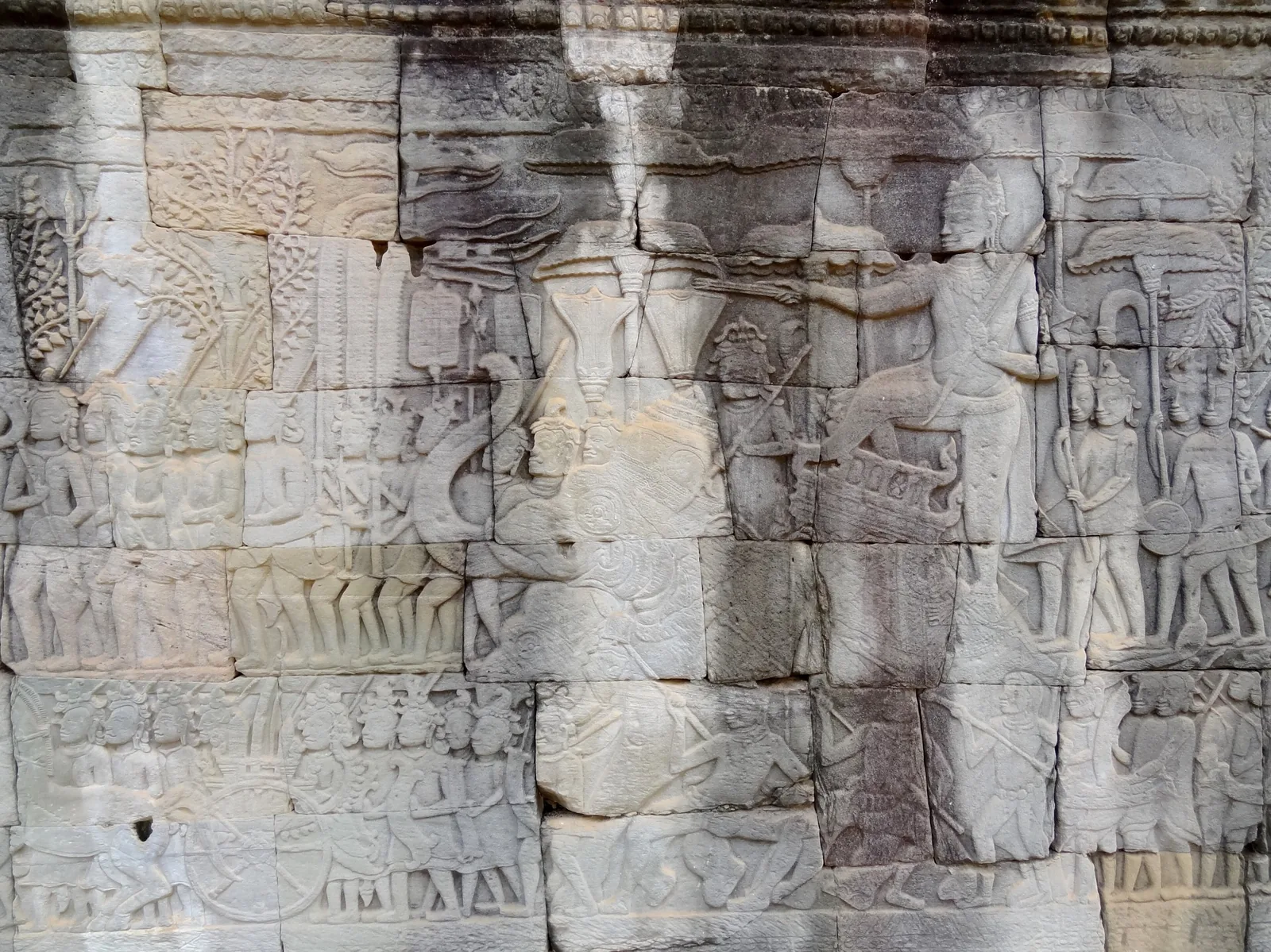 Ancient stone bas-relief carvings depicting figures and battle scenes on a temple wall at Bayon, Angkor Thom.
