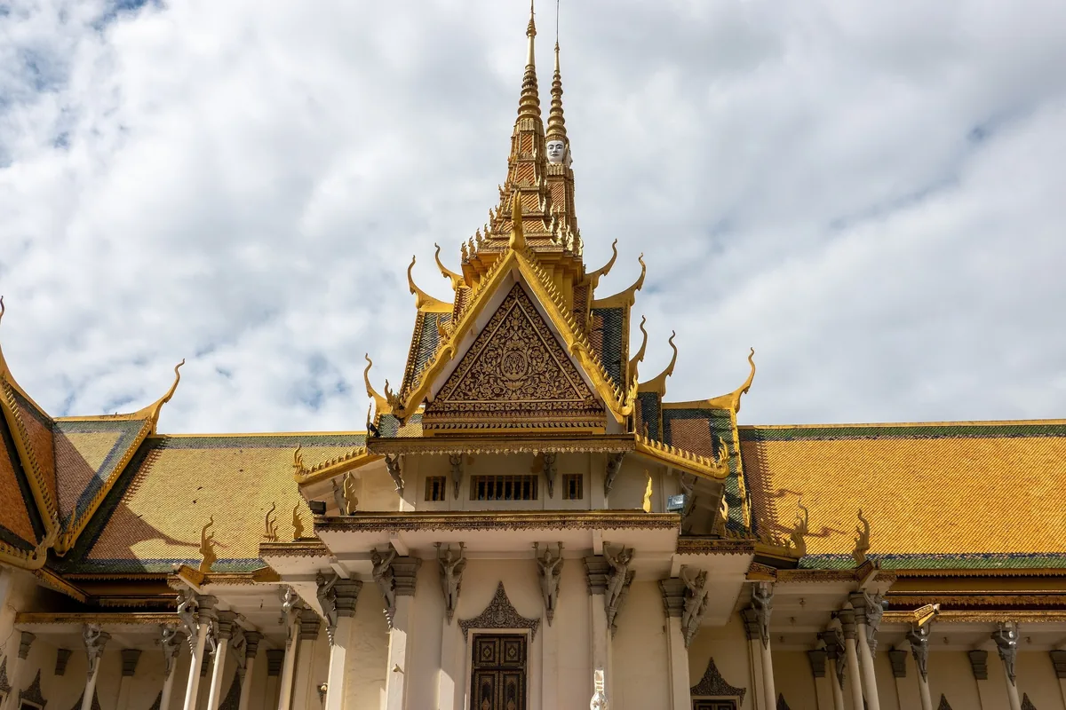 Golden tiered roof and spire of the Throne Hall at the Royal Palace in Phnom Penh under a bright sky.