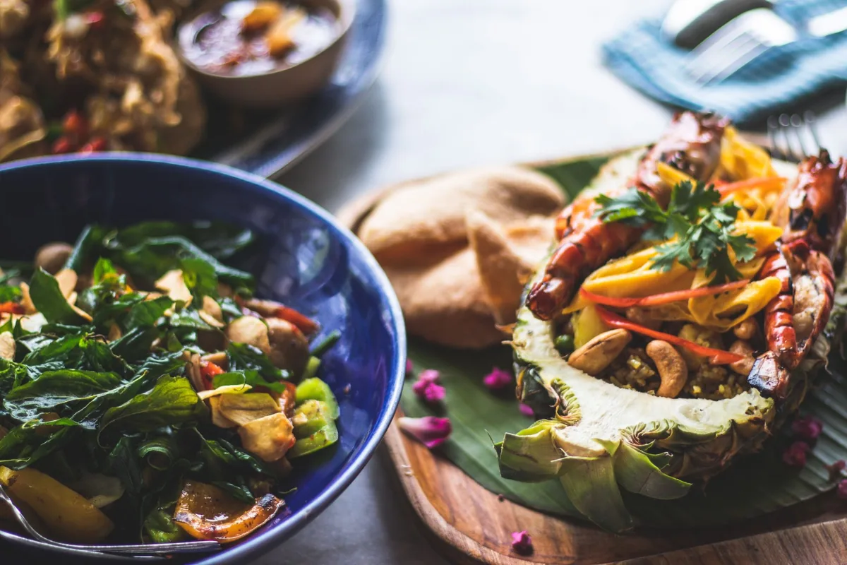 Pineapple fried rice with shrimp served alongside a stir-fried green salad and crispy crackers in Cambodia.