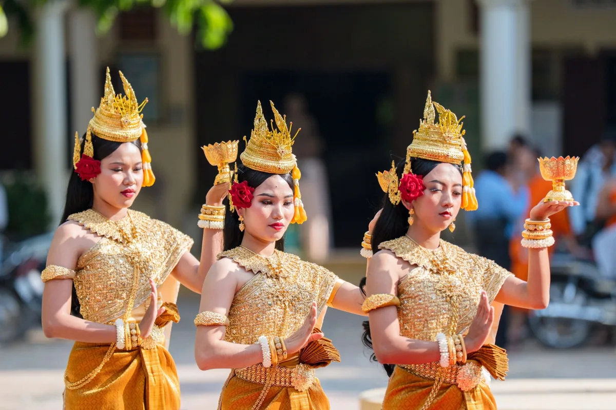 Three Cambodian dancers in golden traditional Khmer costumes and ornate crowns perform a classical Apsara dance.