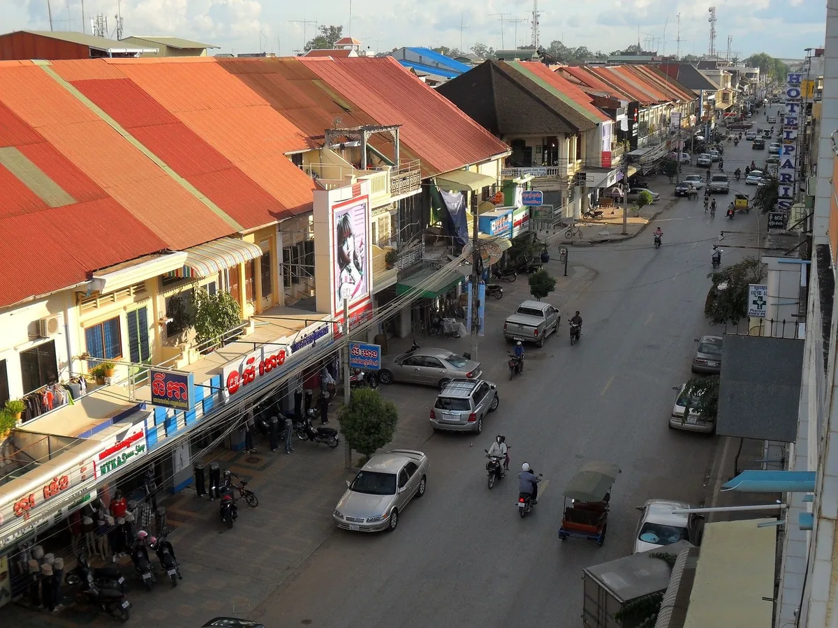 Elevated view of a busy street in Battambang lined with orange-roofed shops, traffic, and motorbikes.