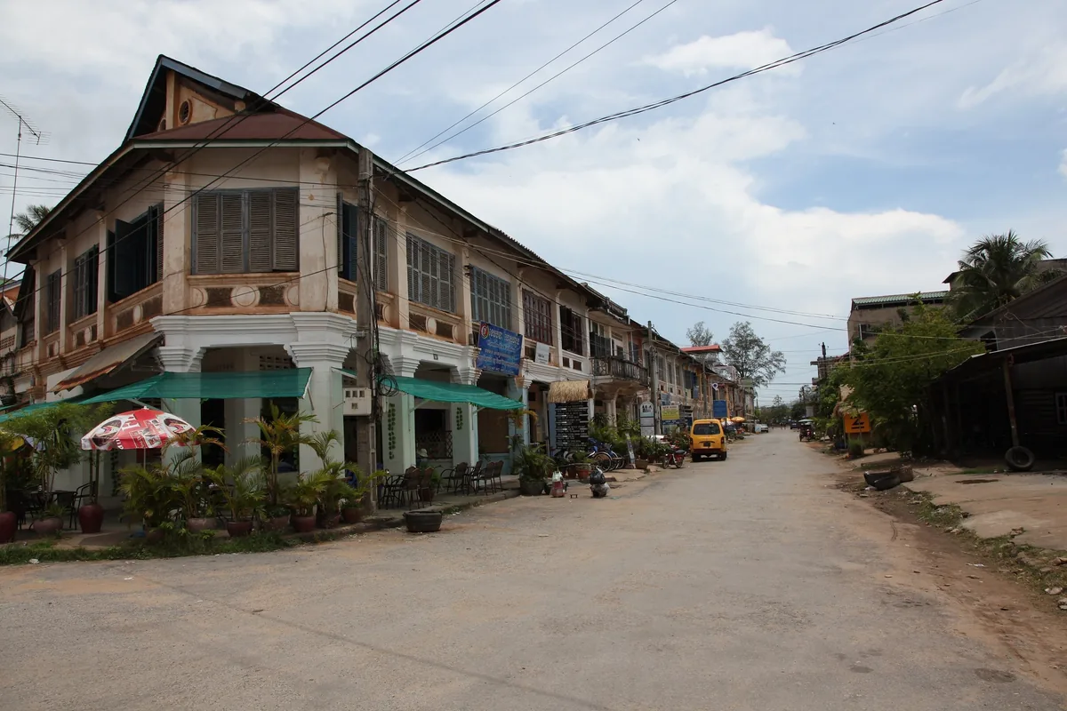 Colonial-era shophouses line a quiet street with overhead wires in Kampot, Cambodia.