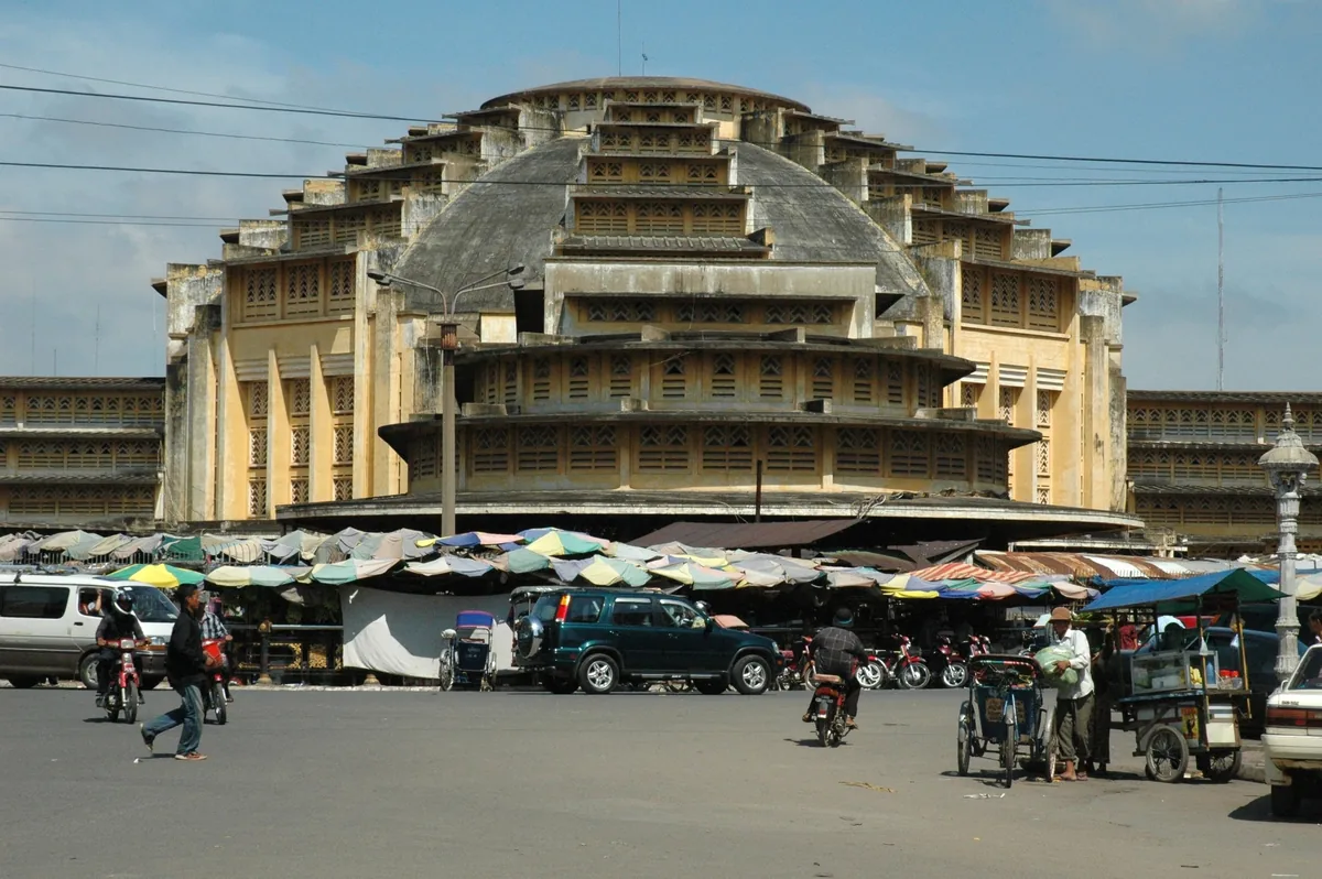 The domed art deco facade of Phsar Thmei (Central Market) rises above a busy street market in Phnom Penh.