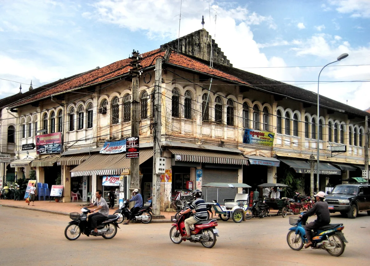Motorbikes pass a colonial-era corner building with red-tiled roof in downtown Siem Reap, Cambodia.