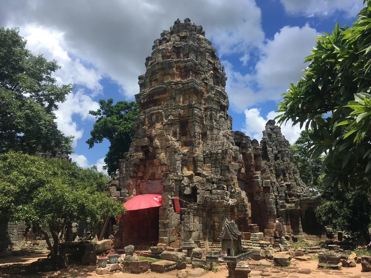 A weathered stone temple tower rises among trees at Phnom Banan in Battambang, Cambodia.