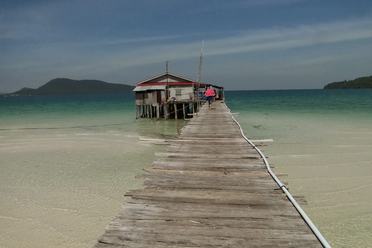 A wooden pier stretches over turquoise water to a stilt house near Koh Rong, Sihanoukville.