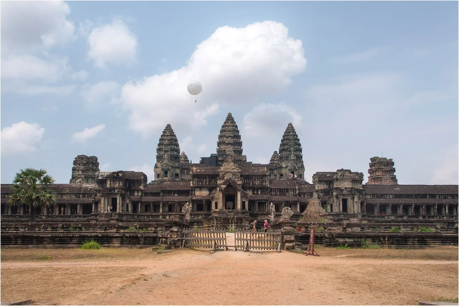 The stone towers of Angkor Wat rise beneath a bright sky with a hot air balloon overhead in Siem Reap.