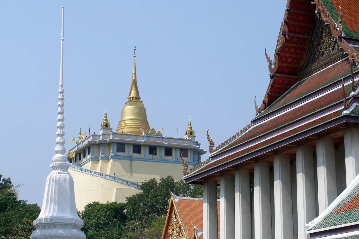 Golden Mount stupa of Wat Saket rises above a temple's tiered roof in Bangkok, Thailand.