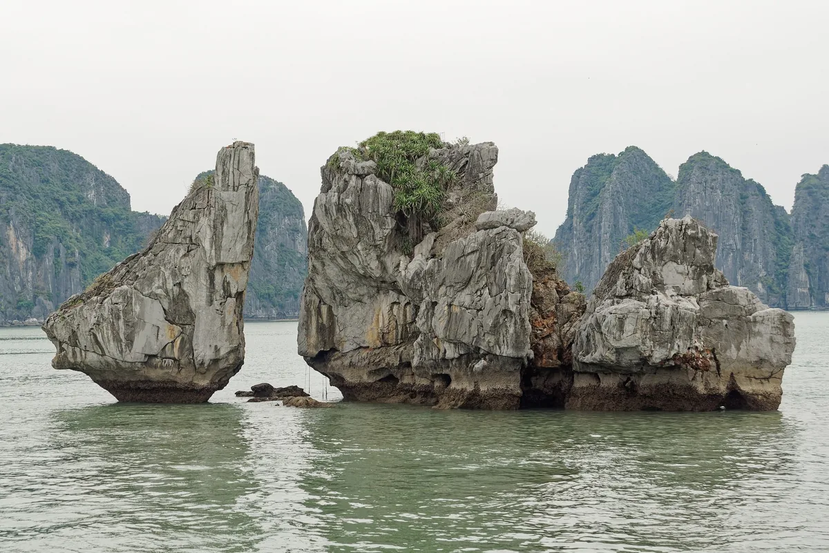 Jagged limestone karsts rise from calm green water in Ha Long Bay, Vietnam.