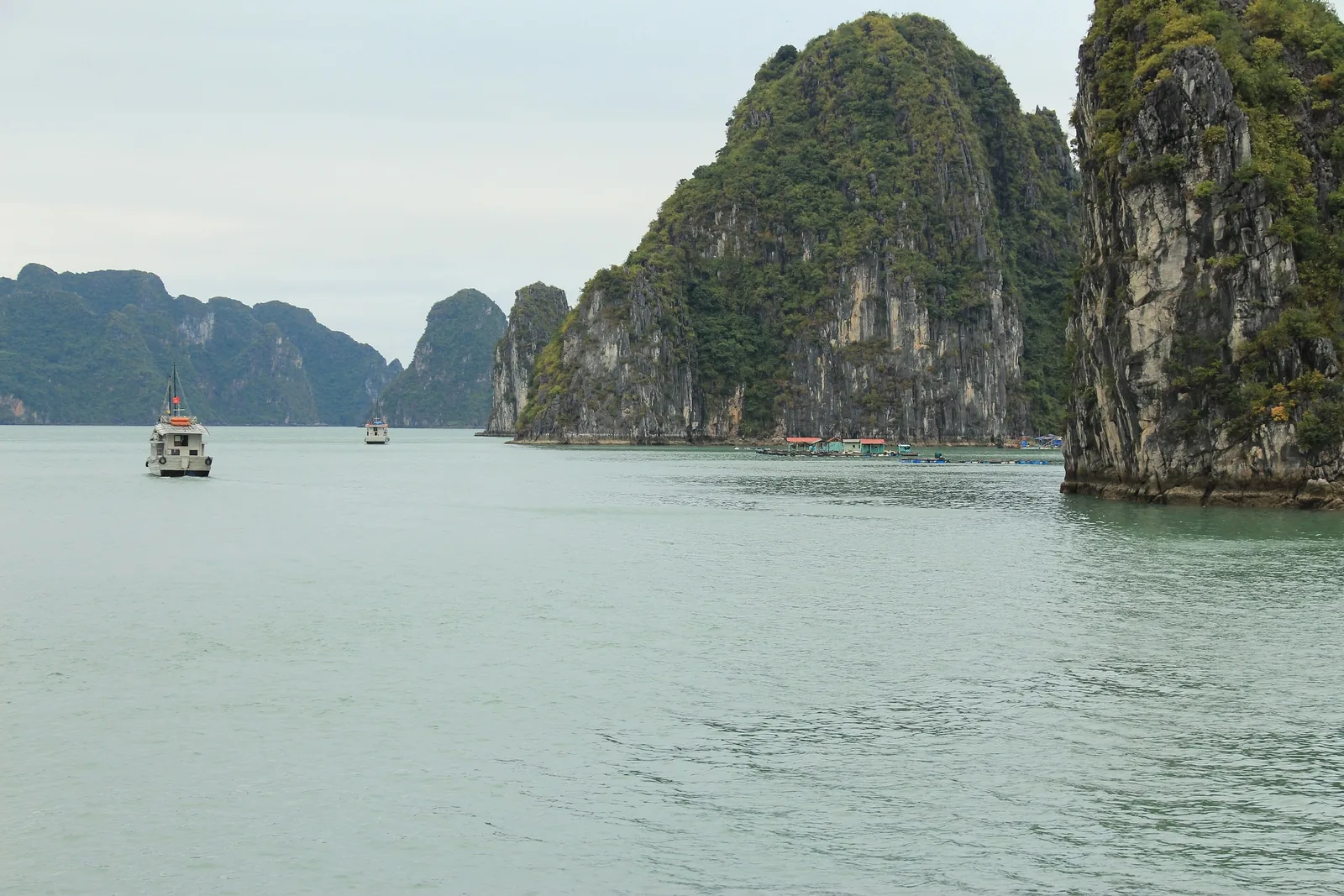 Limestone karsts rise over calm waters as a small boat cruises through Ha Long Bay.