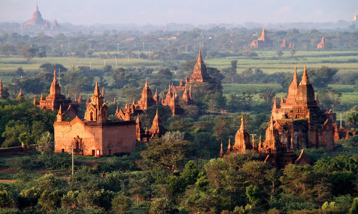 Ancient brick temples and pagodas rise from green plains in Bagan under golden morning light.