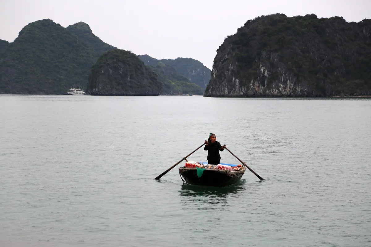 A vendor rows a small wooden boat between limestone karsts in Ha Long Bay.
