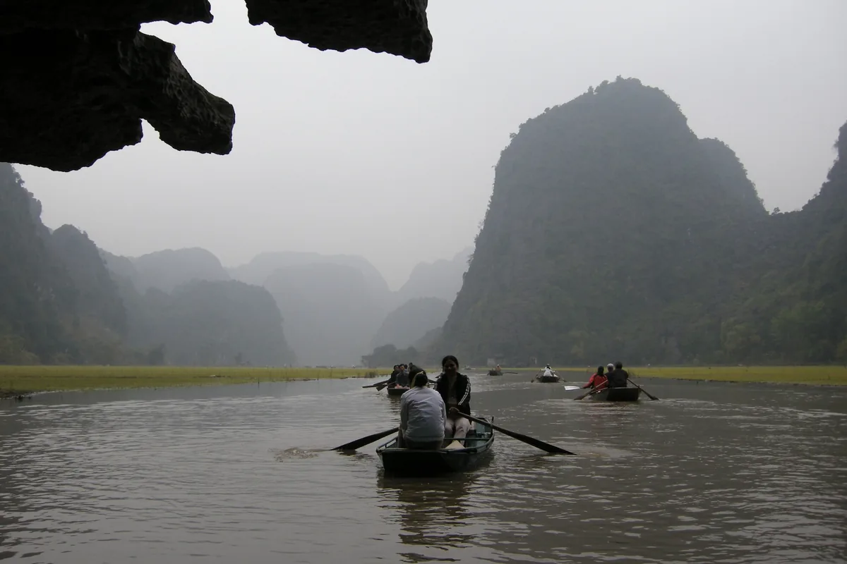 Rowboats carry visitors through a misty river gorge flanked by limestone karsts in Ninh Binh.