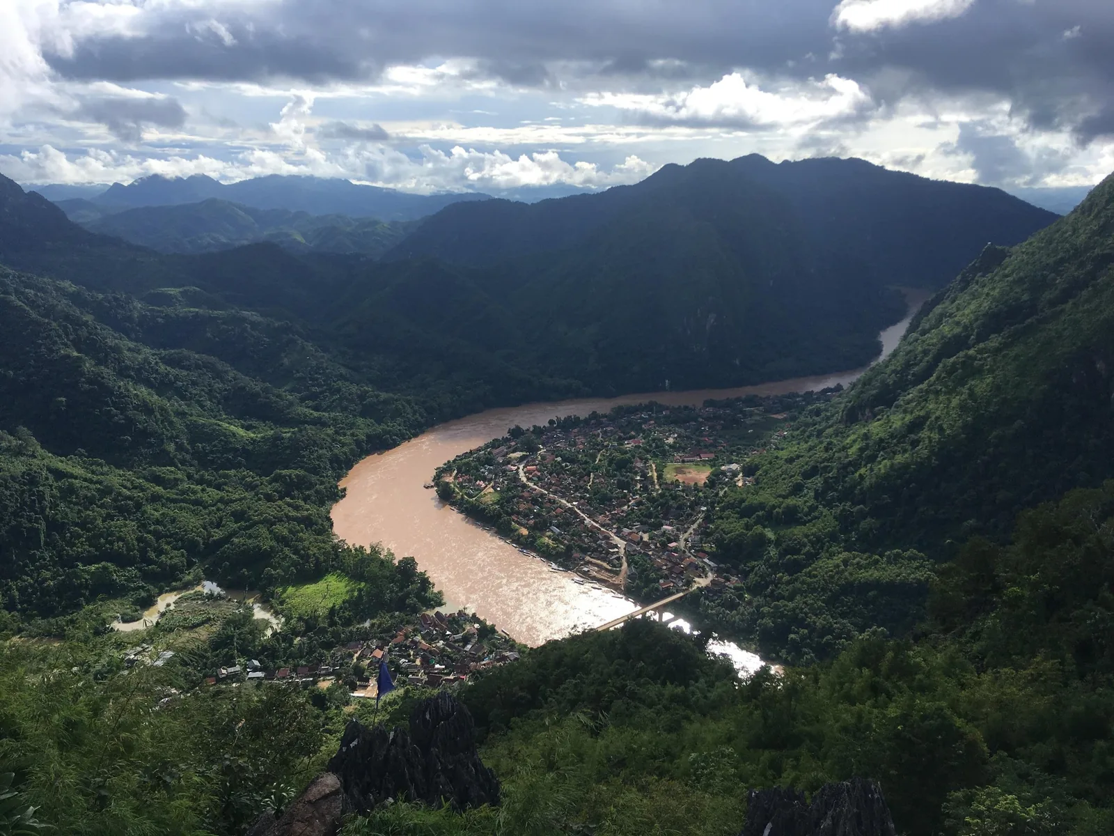Aerial view from a viewpoint over Nong Khiaw village, the muddy river bend, and surrounding limestone mountains in Laos.