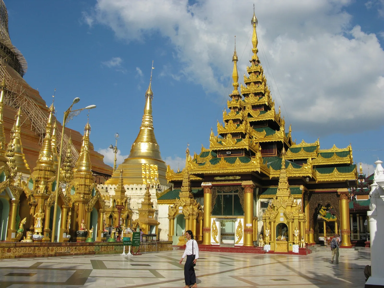 Golden spires and pavilions surround the marble terrace of Shwedagon Pagoda in Yangon under a blue sky.