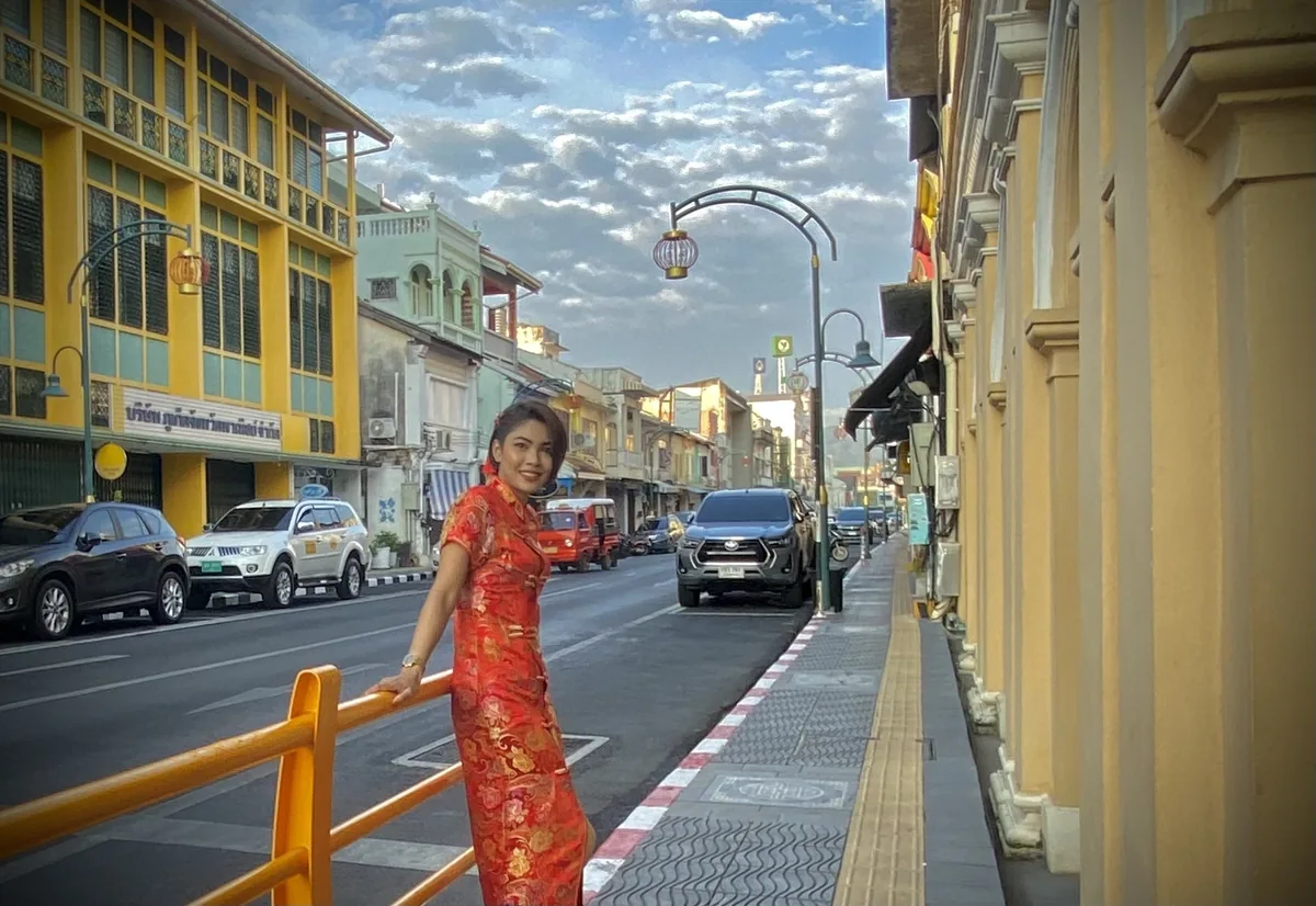 A woman in a red qipao poses along a colonial-style shophouse street in Phuket Old Town.