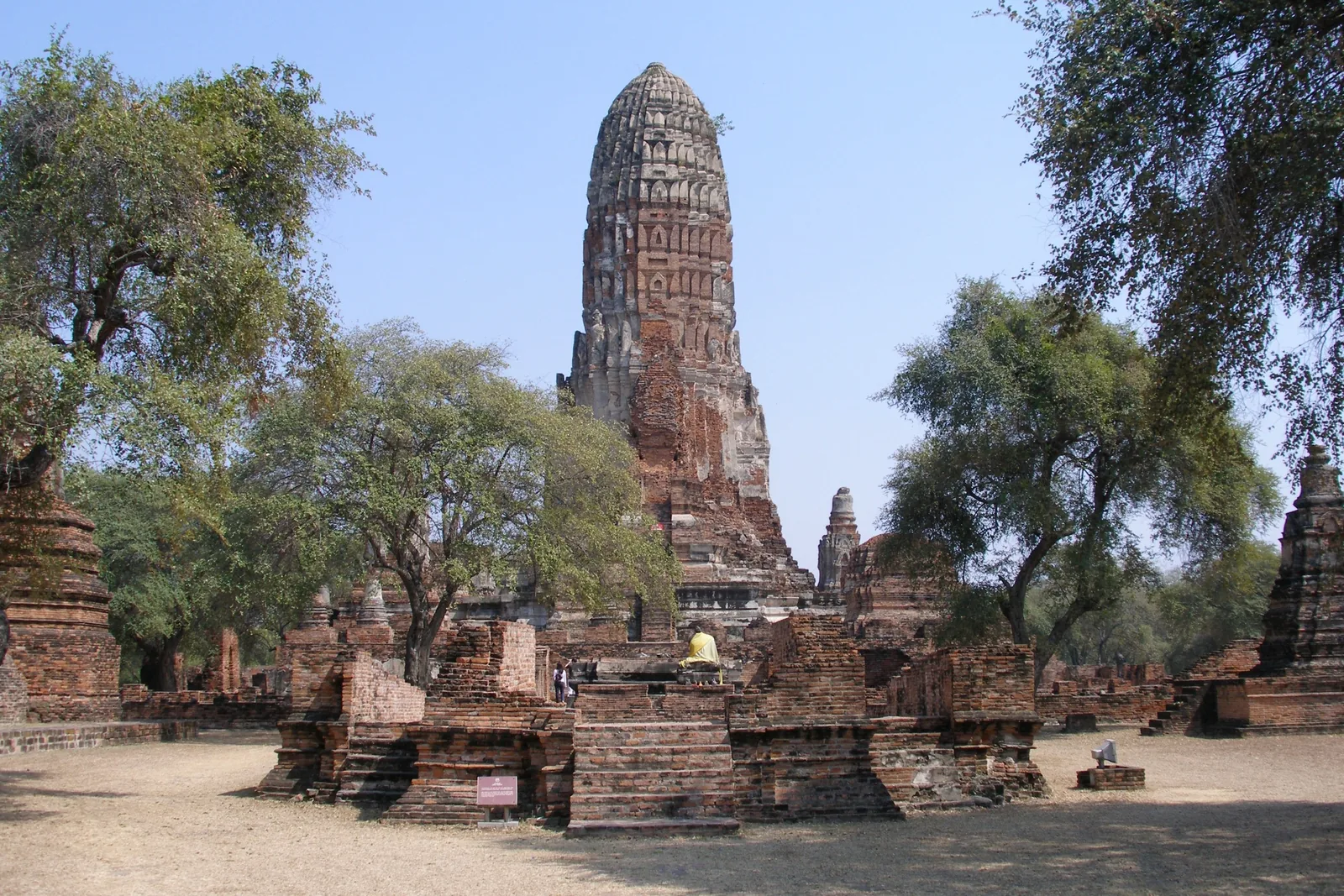 A tall brick prang temple ruin rises among trees at a historic site in Ayutthaya, Thailand.