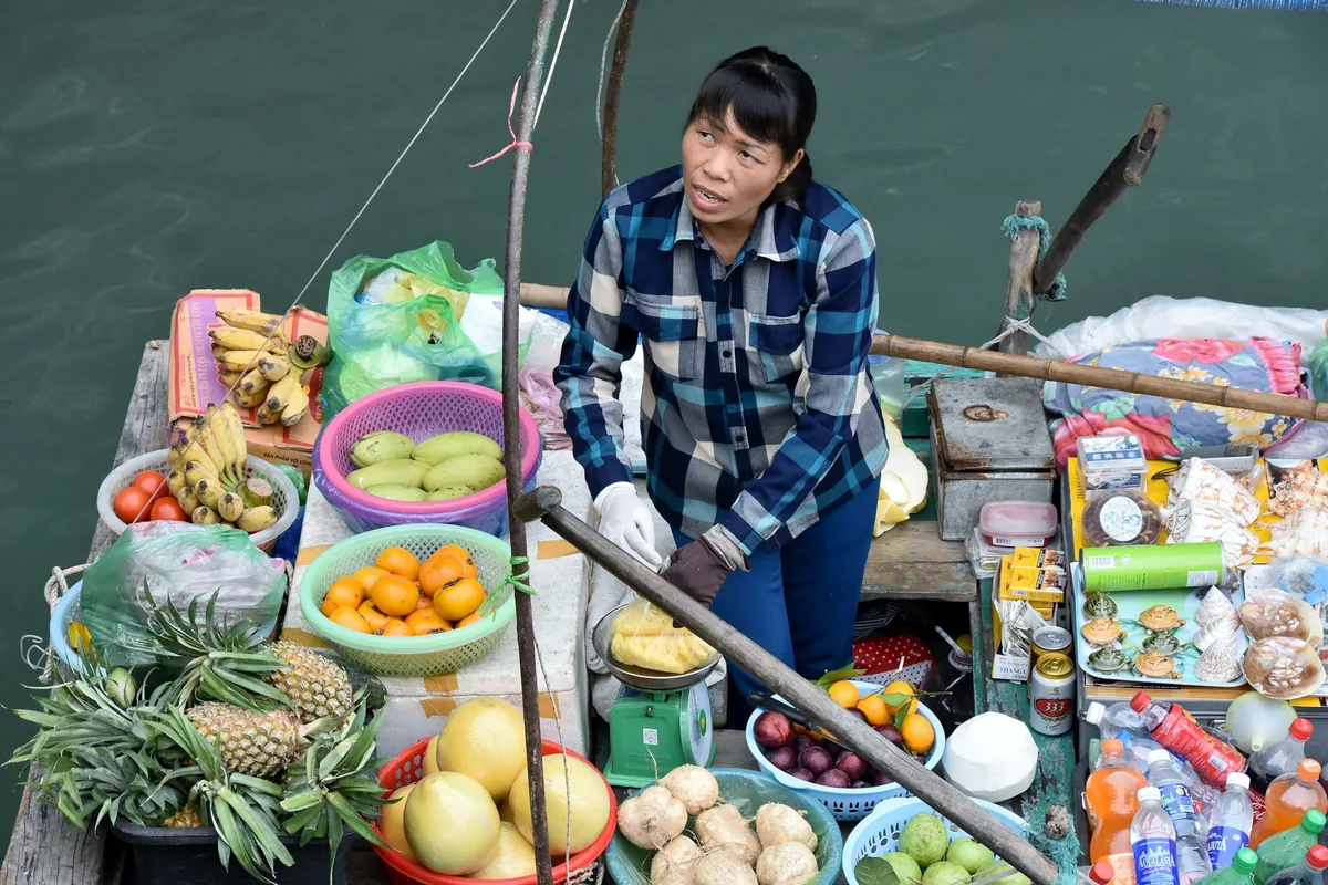 A woman on a floating vendor boat sells fresh fruit and snacks on Ha Long Bay's waters.