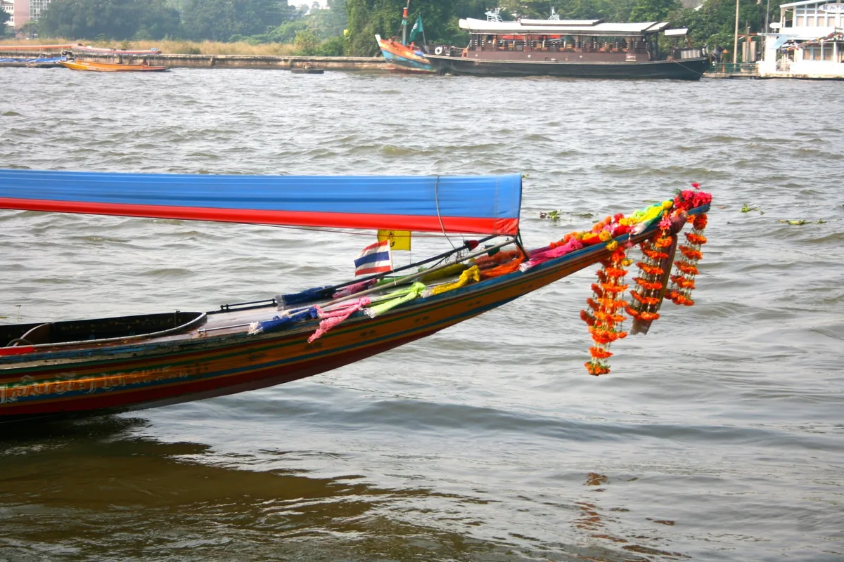 A colorful long-tail boat with floral garlands and a Thai flag floats on the Chao Phraya River in Bangkok.
