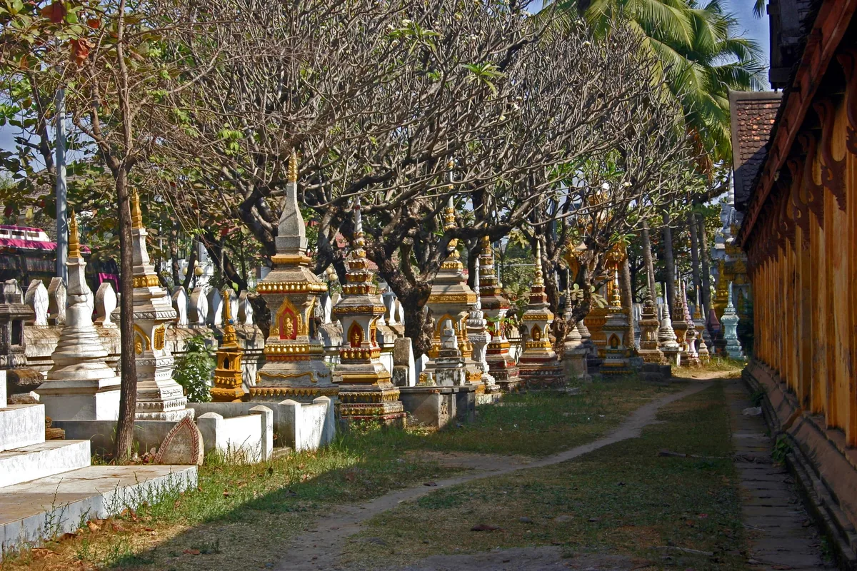 Rows of ornate stupas line a shaded pathway beside a temple at Wat Sisaket in Vientiane.