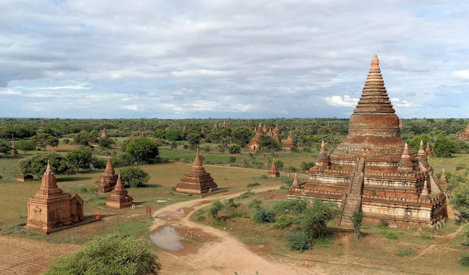 Ancient brick temples and stupas rise across the green plains of Bagan under a wide sky.