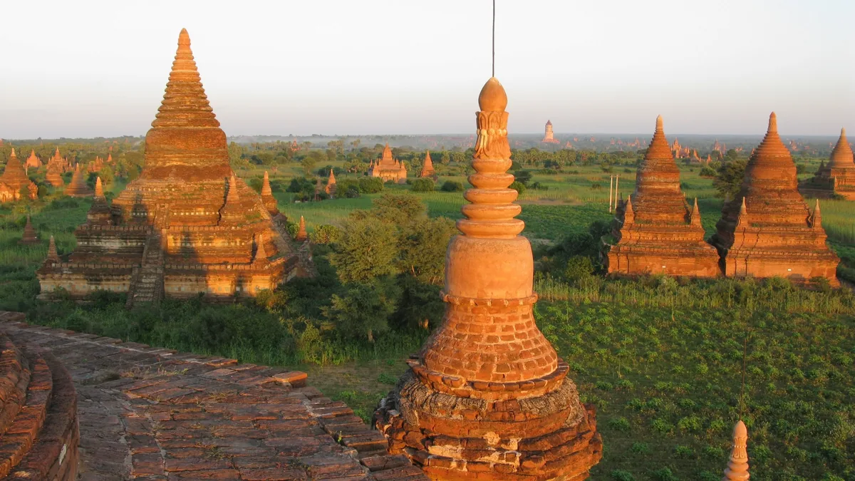Ancient brick temples and stupas scattered across the plains of Bagan glow orange at sunset.