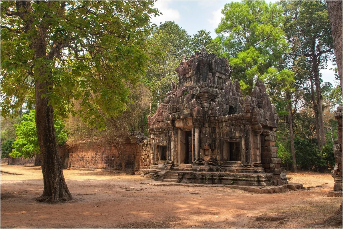 An ancient stone temple ruin surrounded by tall trees in the Angkor Thom complex near Siem Reap.