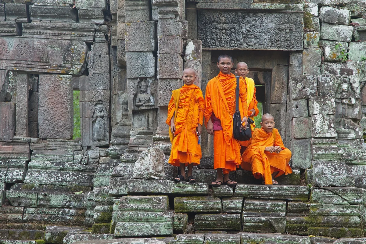 Buddhist monks in saffron robes stand among ancient stone ruins at Preah Pithu near Siem Reap.