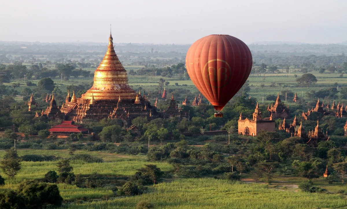 A hot air balloon drifts near a golden pagoda amid the temple-studded plains of Bagan.