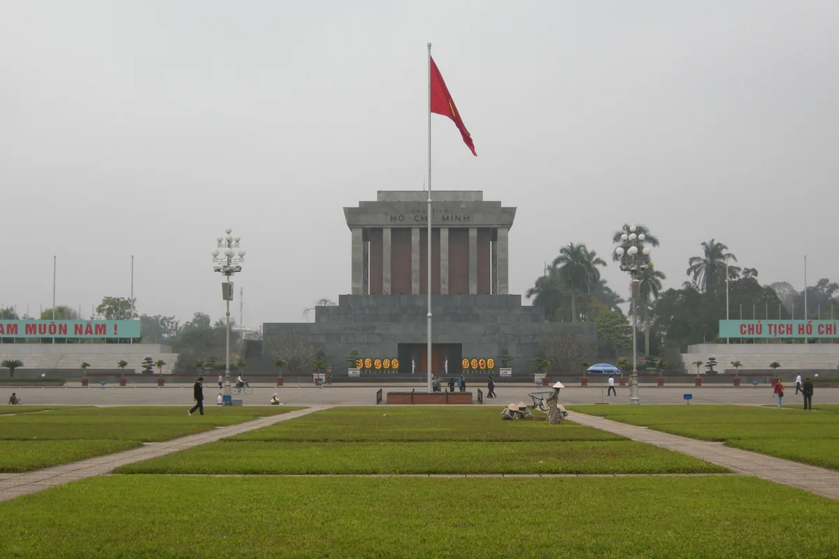 Ho Chi Minh Mausoleum stands beyond a red flag and green lawns in Hanoi's Ba Dinh Square.