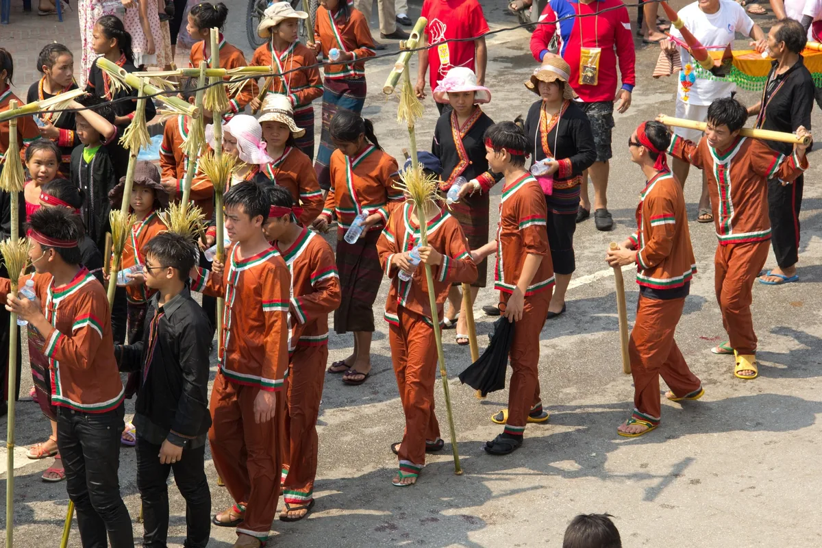 Performers in traditional brown costumes carry bamboo poles during a street procession in Luang Prabang.