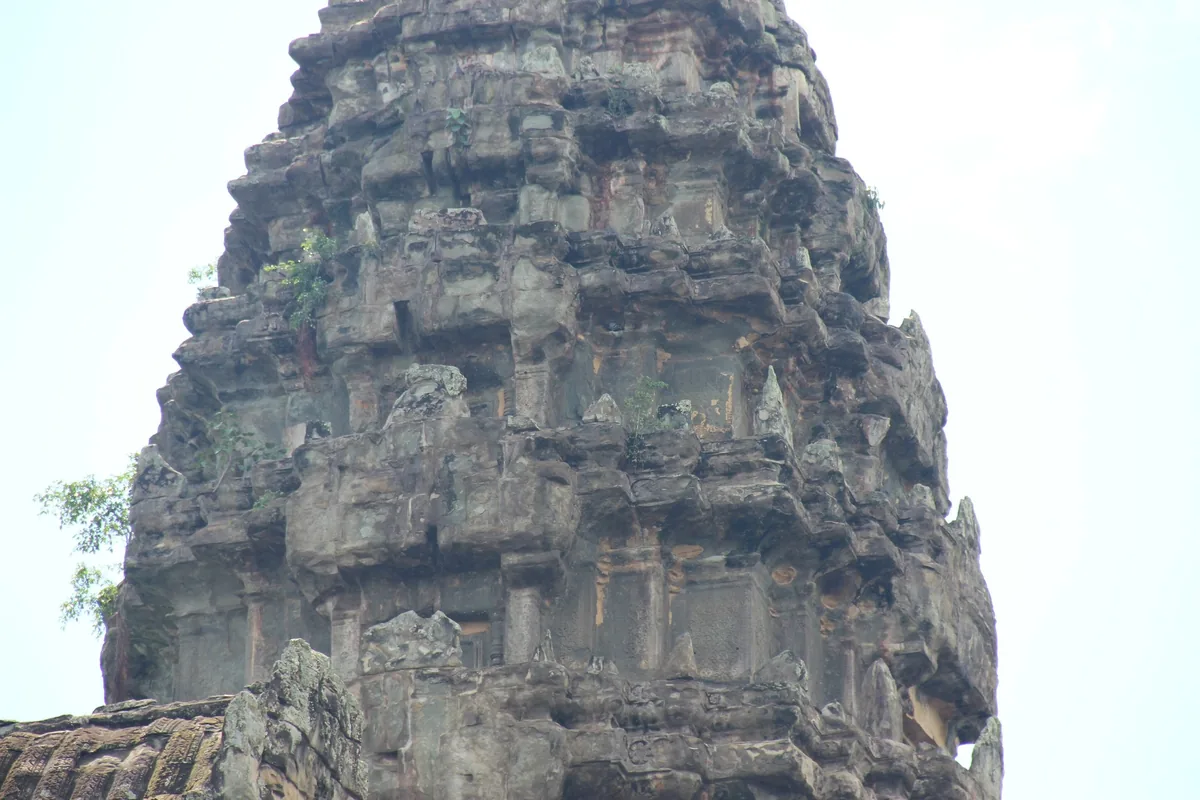 A weathered stone tower of Angkor Wat rises against a pale sky in Siem Reap, Cambodia.