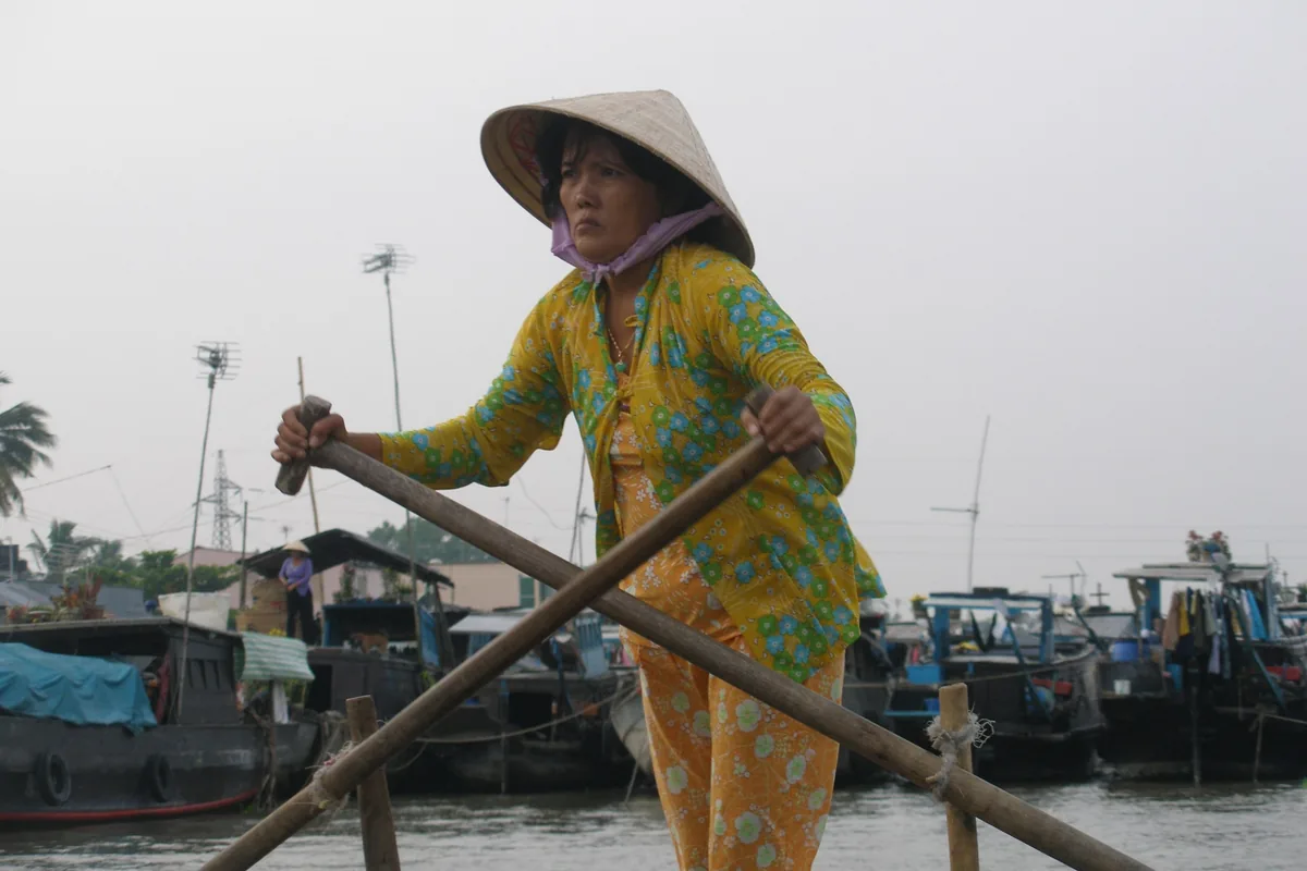 A woman in a conical hat rows a wooden boat through the floating market in Can Tho.
