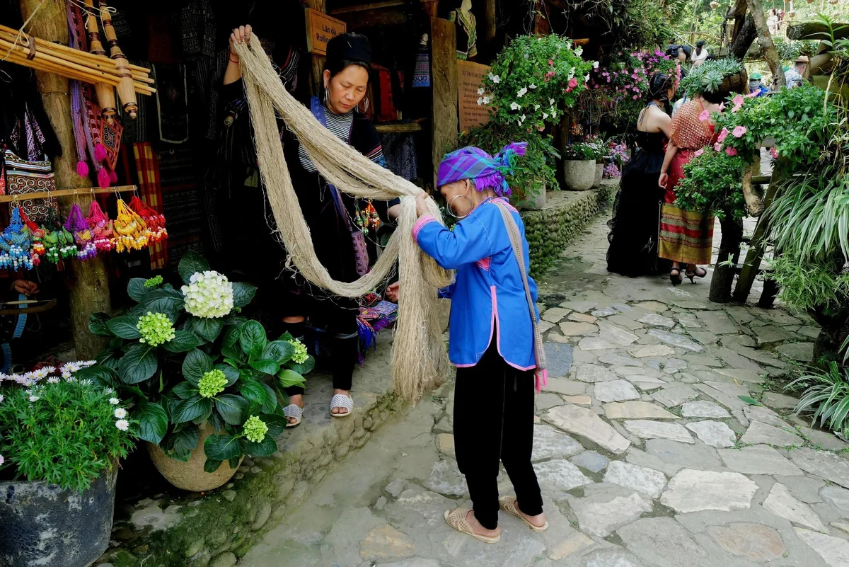 Hmong women in traditional dress handle hemp fiber threads at a craft stall in Cat Cat Village, Sapa.