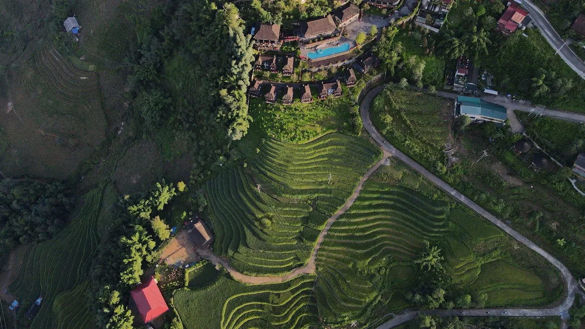 Aerial view of terraced tea fields curving beside a hillside resort with pool near Sapa, Vietnam.