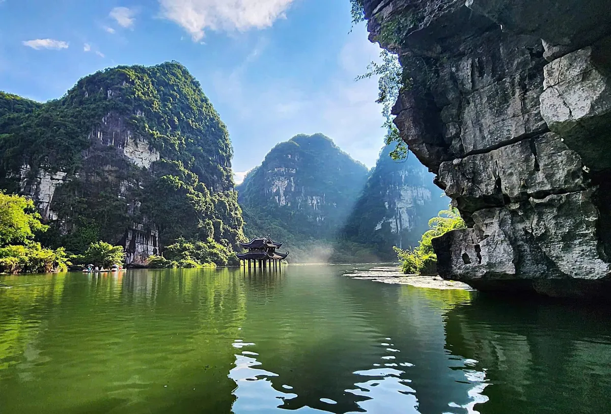 Limestone karsts tower over a calm green river with a small pagoda in Ninh Binh, Vietnam.