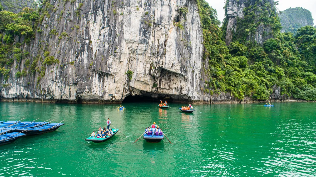 Small rowboats carry tourists across emerald waters beneath towering limestone karsts in Lan Ha Bay.
