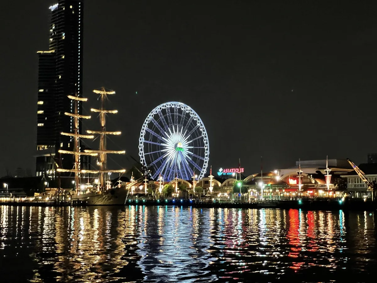 The illuminated Ferris wheel and Asiatique riverfront market glow at night along Bangkok's Chao Phraya River.