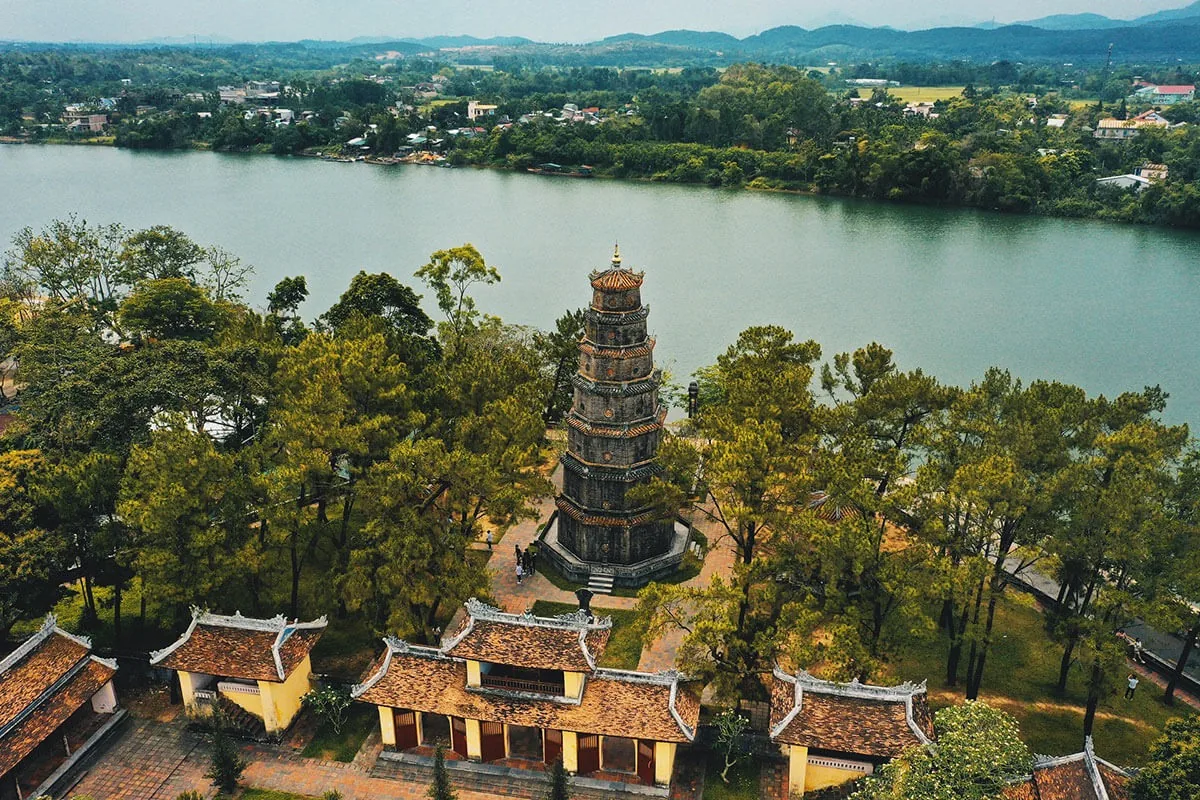 Aerial view of Thien Mu Pagoda's tiered tower rising above trees beside the Perfume River in Hue.