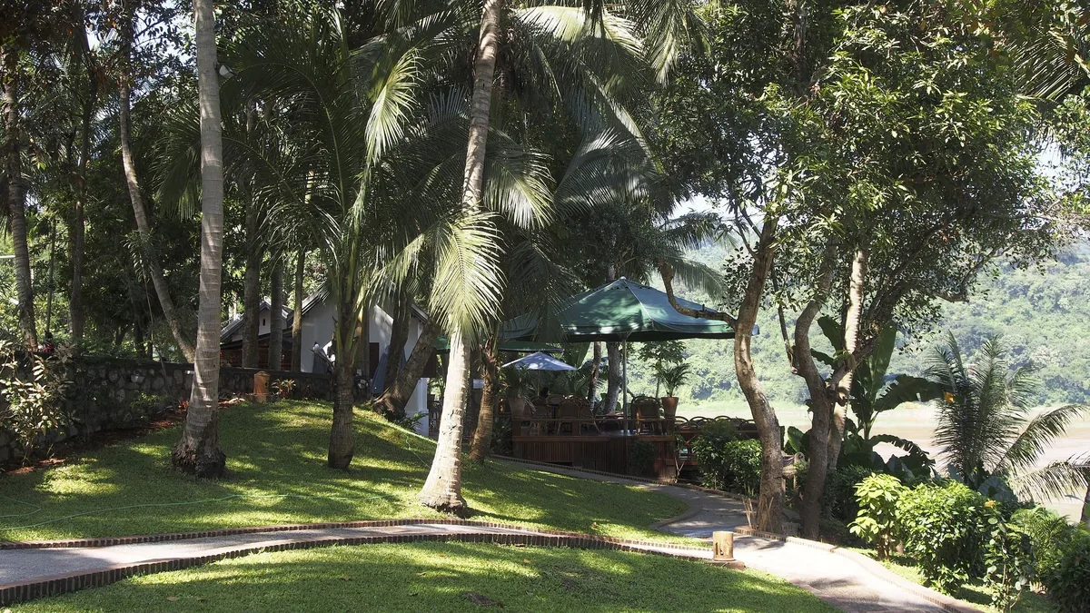 Palm trees shade a riverside garden terrace with umbrellas at a resort in Luang Prabang.