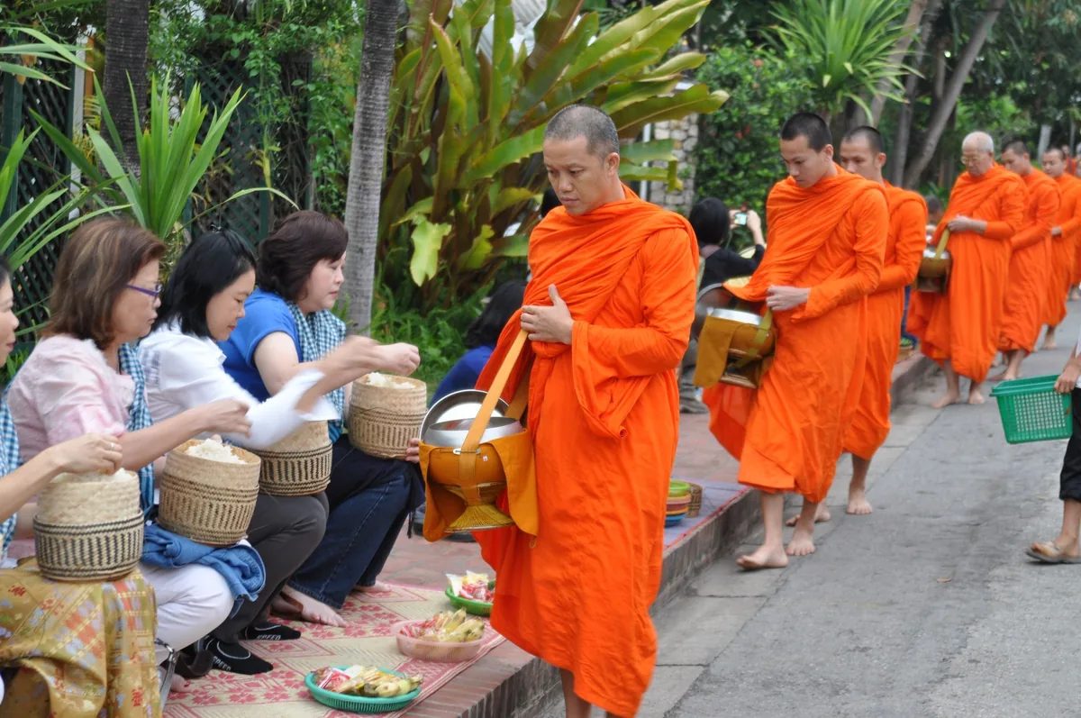 Buddhist monks in orange robes collect alms from local women along a street in Luang Prabang.