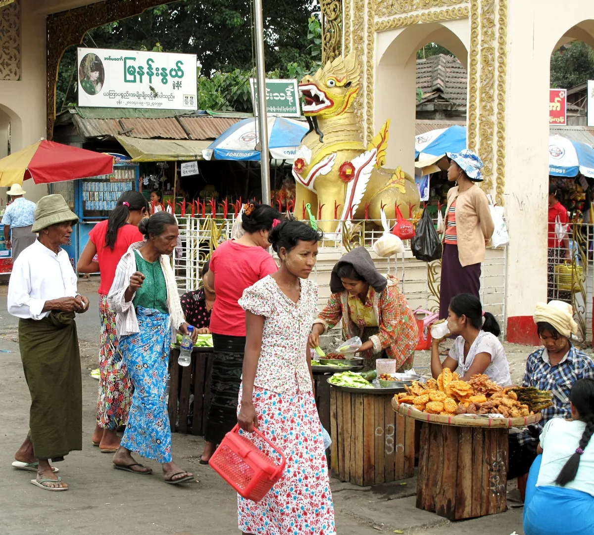 Local vendors sell food and goods near a golden lion statue at a temple gate in Yangon
