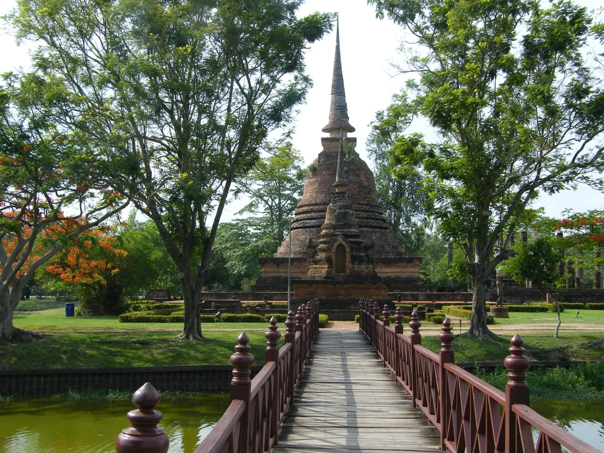 A wooden bridge leads across a moat to an ancient brick chedi at Sukhothai Historical Park.