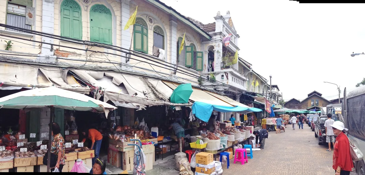 Vendors sell goods under canopies along a street lined with old colonial-style shophouses in Bangkok.