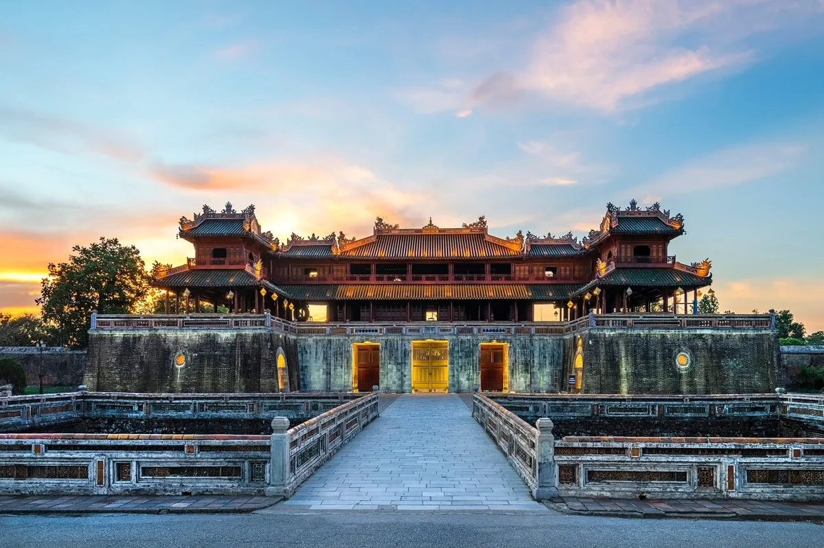 Sunset glows behind the ornate gate and stone bridge of the Imperial City in Hue, Vietnam.