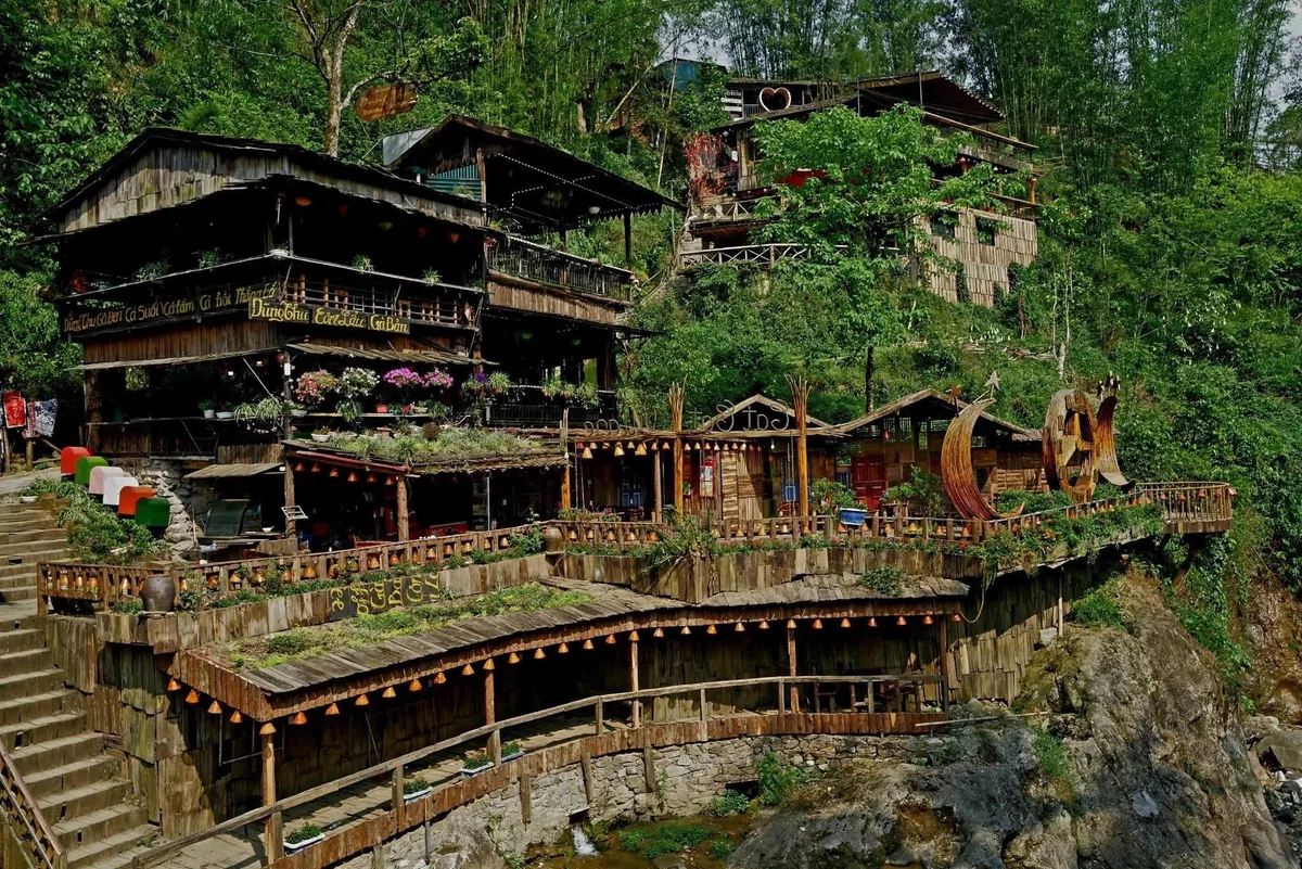 Wooden houses and terraces cling to a green hillside above a stream in Cat Cat Village.